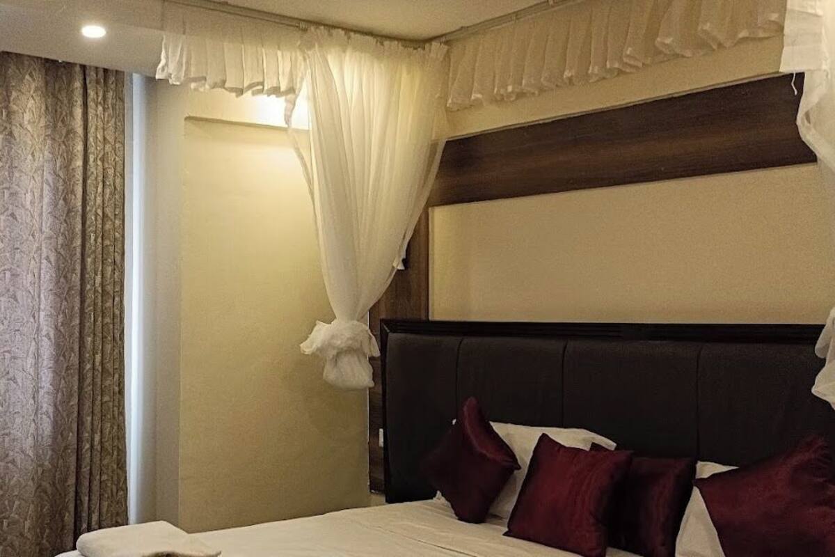 Ein Hotelzimmer mit einem großen Bett, einem dunklen Kopfteil und einem Fenster mit Vorhängen.