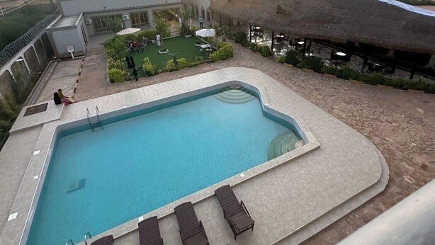 A rooftop pool with lounge chairs, a small garden area, and a view of the sunset.