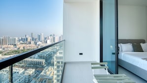 A balcony with a city view, a bed with a grey headboard, and a glass door leading to a bedroom. - PVH - Cozy 1BR - Binghatti House (Dubai)