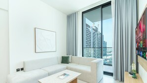 A modern living room with a sofa, a coffee table, and a large window with curtains. - PVH - Cozy 1BR - Binghatti House (Dubai)
