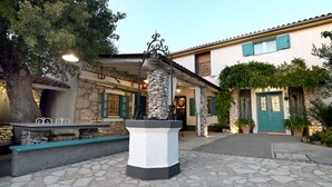 A courtyard with a stone fountain, a bench, and a building with a stone facade and blue shutters. - Villa Buby by Villas Guide (Kraljevica)