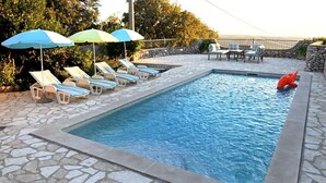 A swimming pool with lounge chairs and umbrellas, surrounded by stone tiles and greenery. - Villa Buby by Villas Guide (Kraljevica)