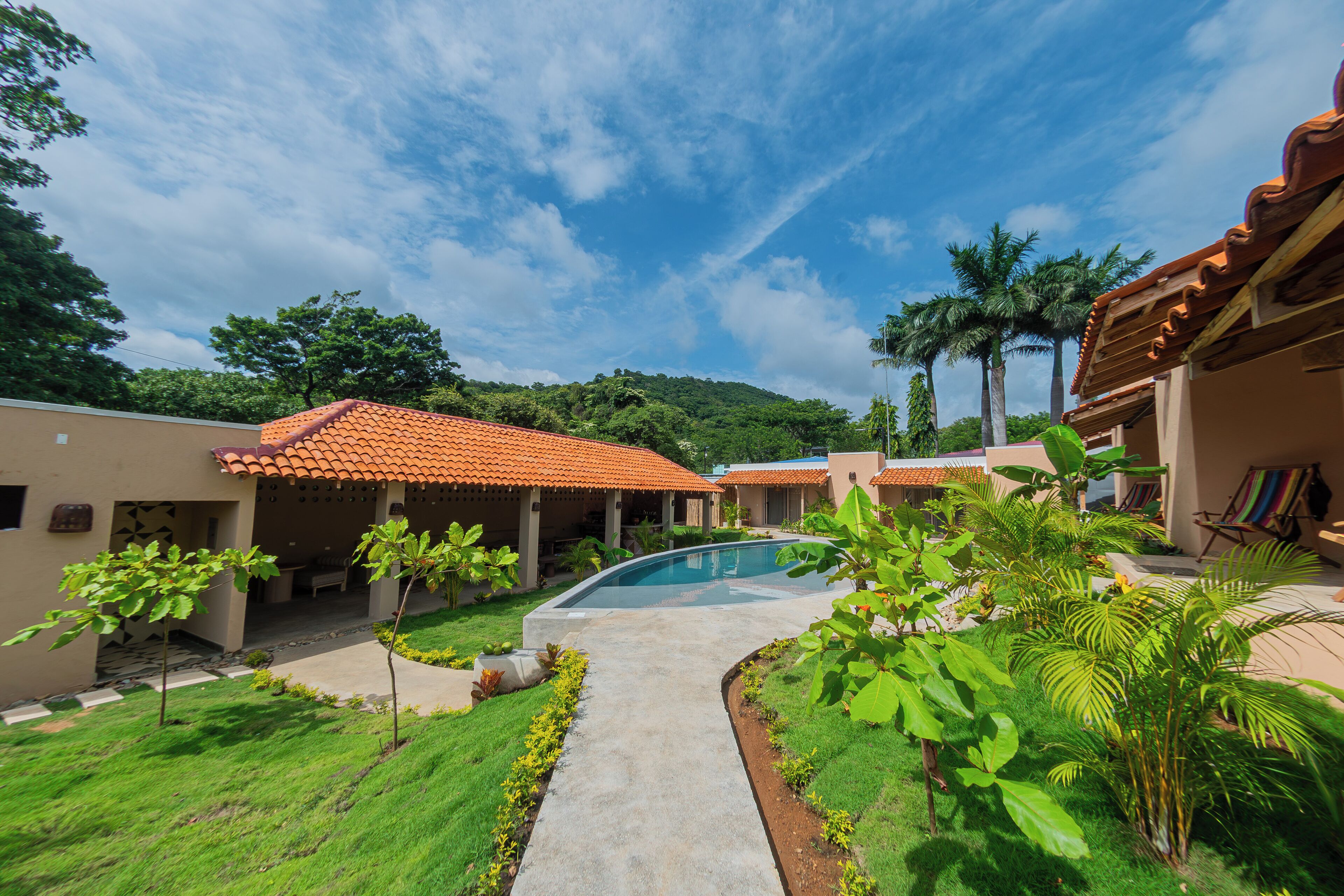 A resort with a swimming pool, palm trees, and a mountainous backdrop.