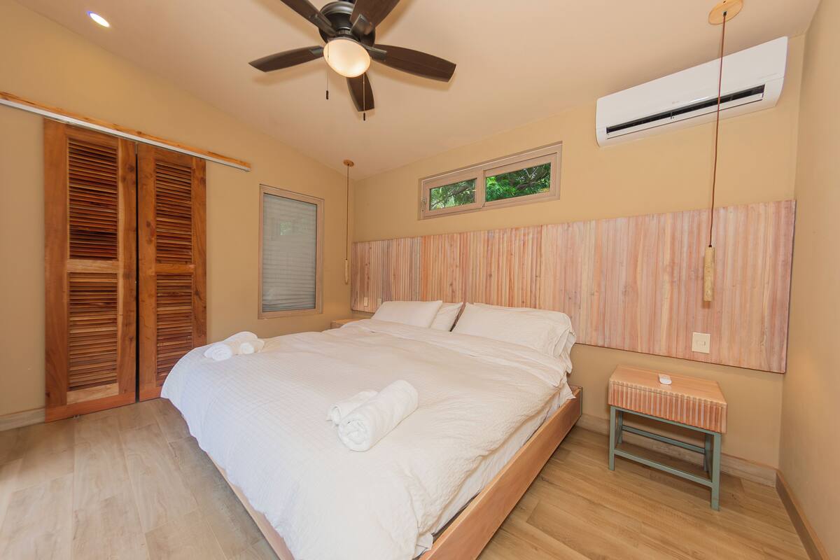 Une chambre à coucher comprenant un lit, une armoire en bois, un ventilateur de plafond, un appareil de climatisation et une petite table de chevet.