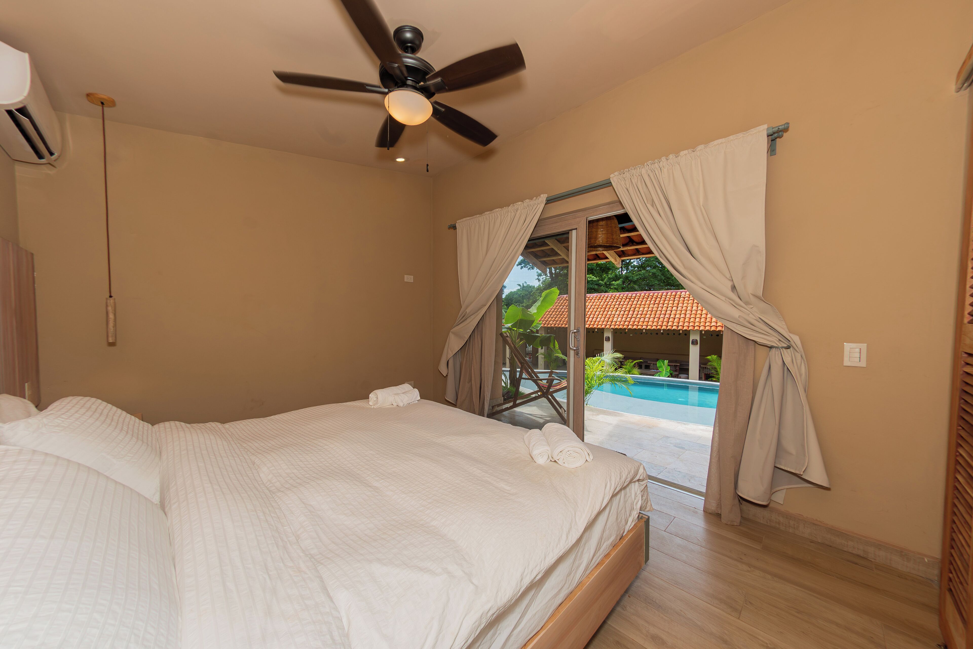A bedroom with a bed, ceiling fan, and a view of a swimming pool.