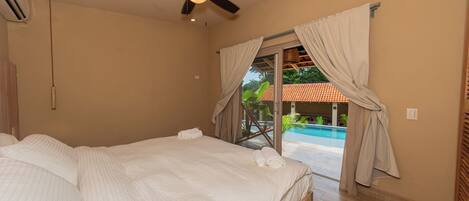 A bedroom with a bed, ceiling fan, and a view of a swimming pool.