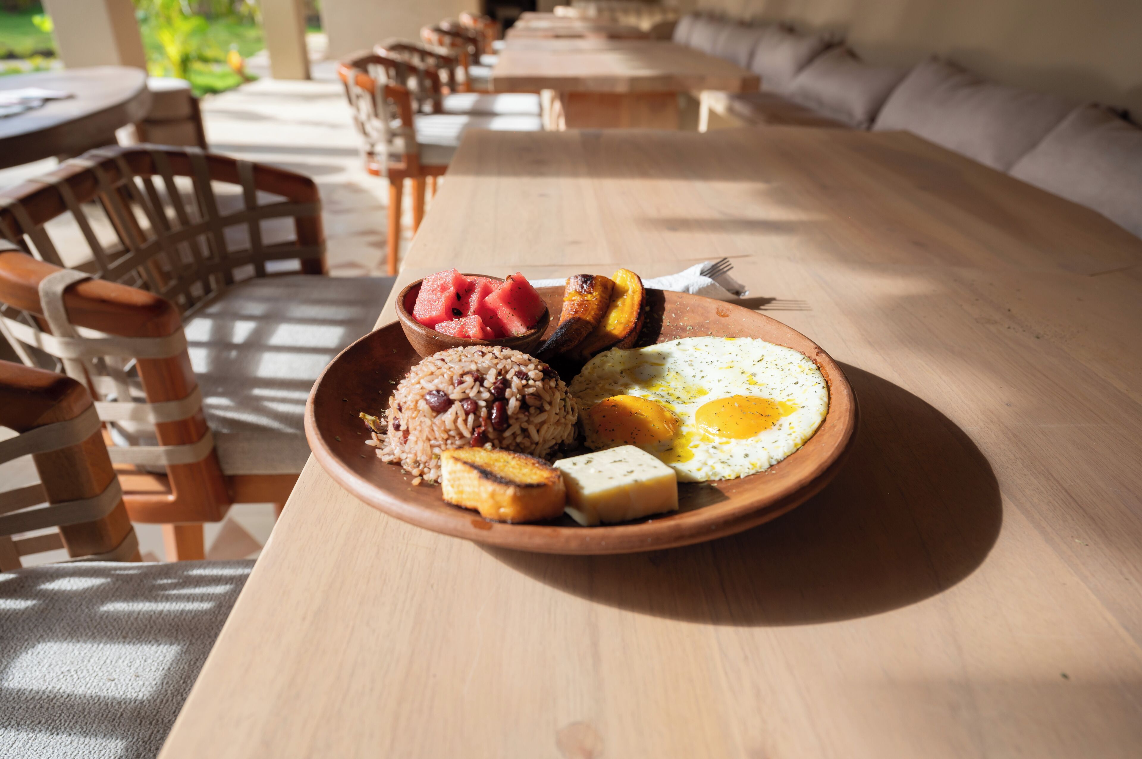 A wooden table with a plate of food including rice, beans, eggs, and fruit.