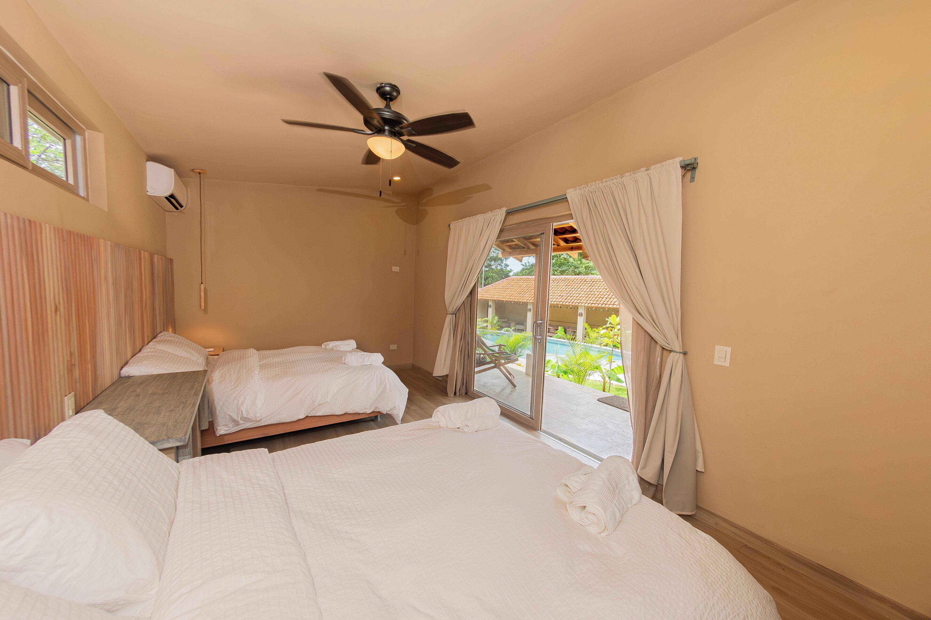 A hotel room with two beds, a ceiling fan, and a sliding glass door leading to an outdoor area.