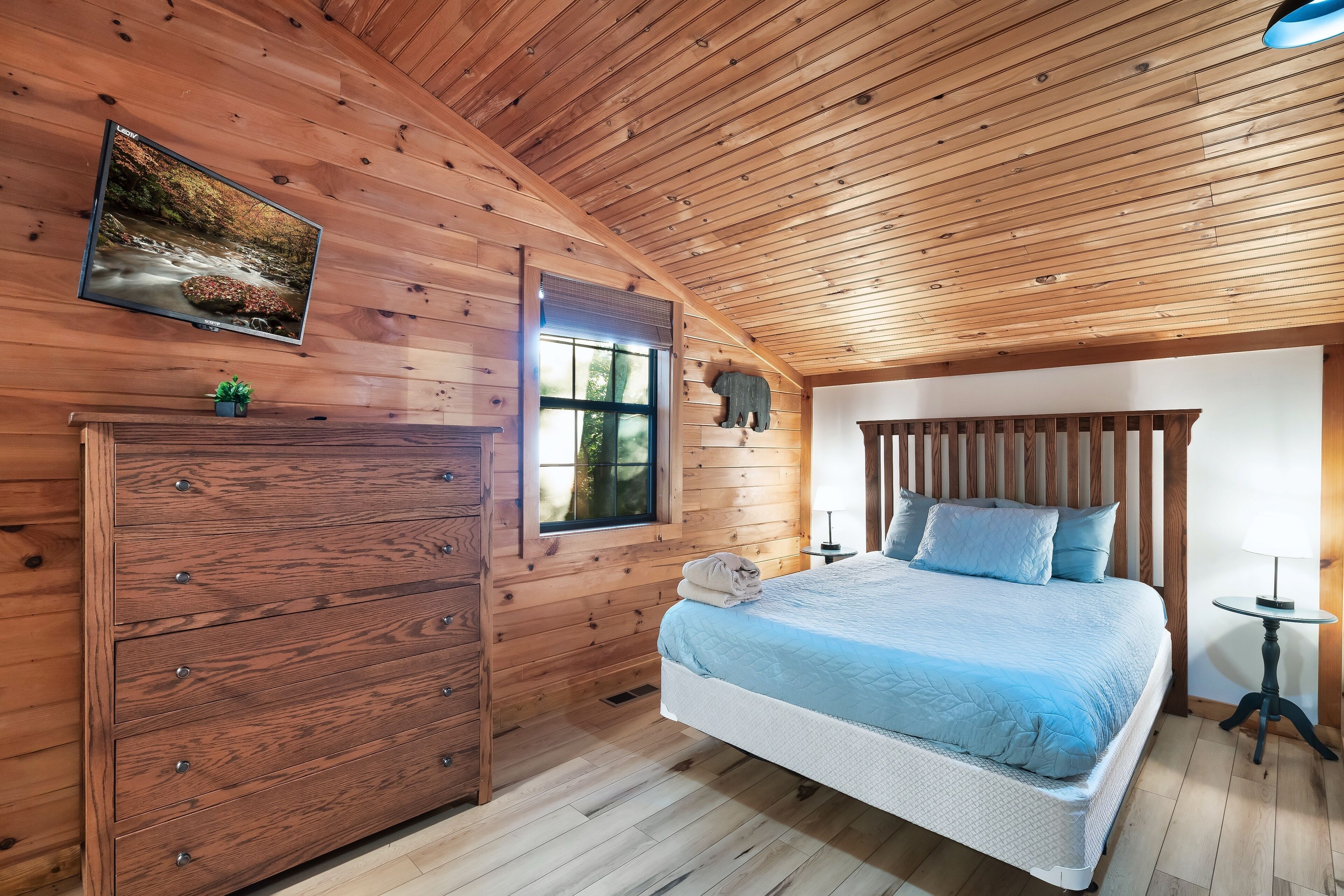 A wooden cabin bedroom with a bed, dresser, and a television mounted on the wall.
