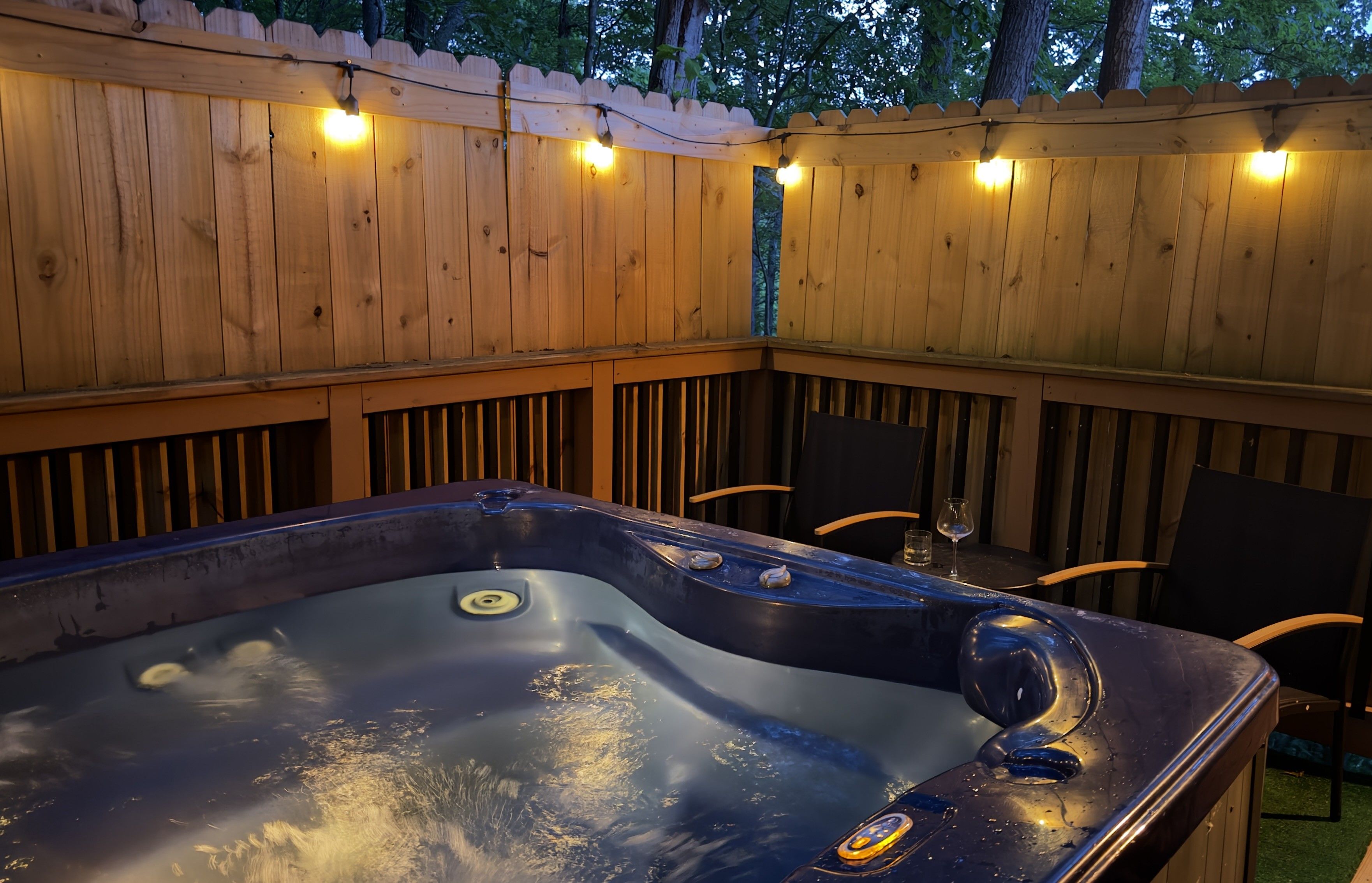 Un jacuzzi con terraza de madera y luces cálidas.