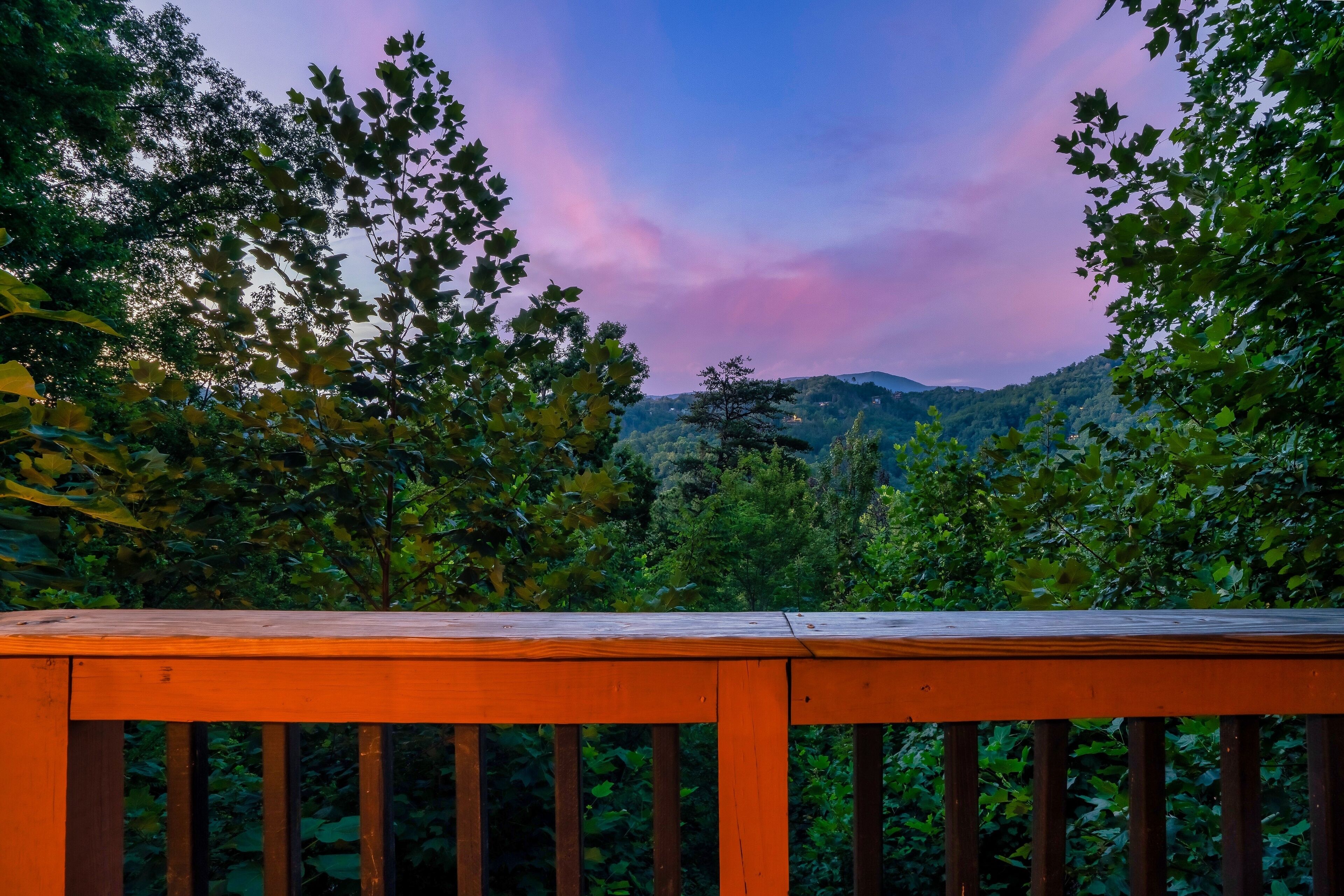 A wooden deck with a view of a forested hillside and a mountain range in the distance.
