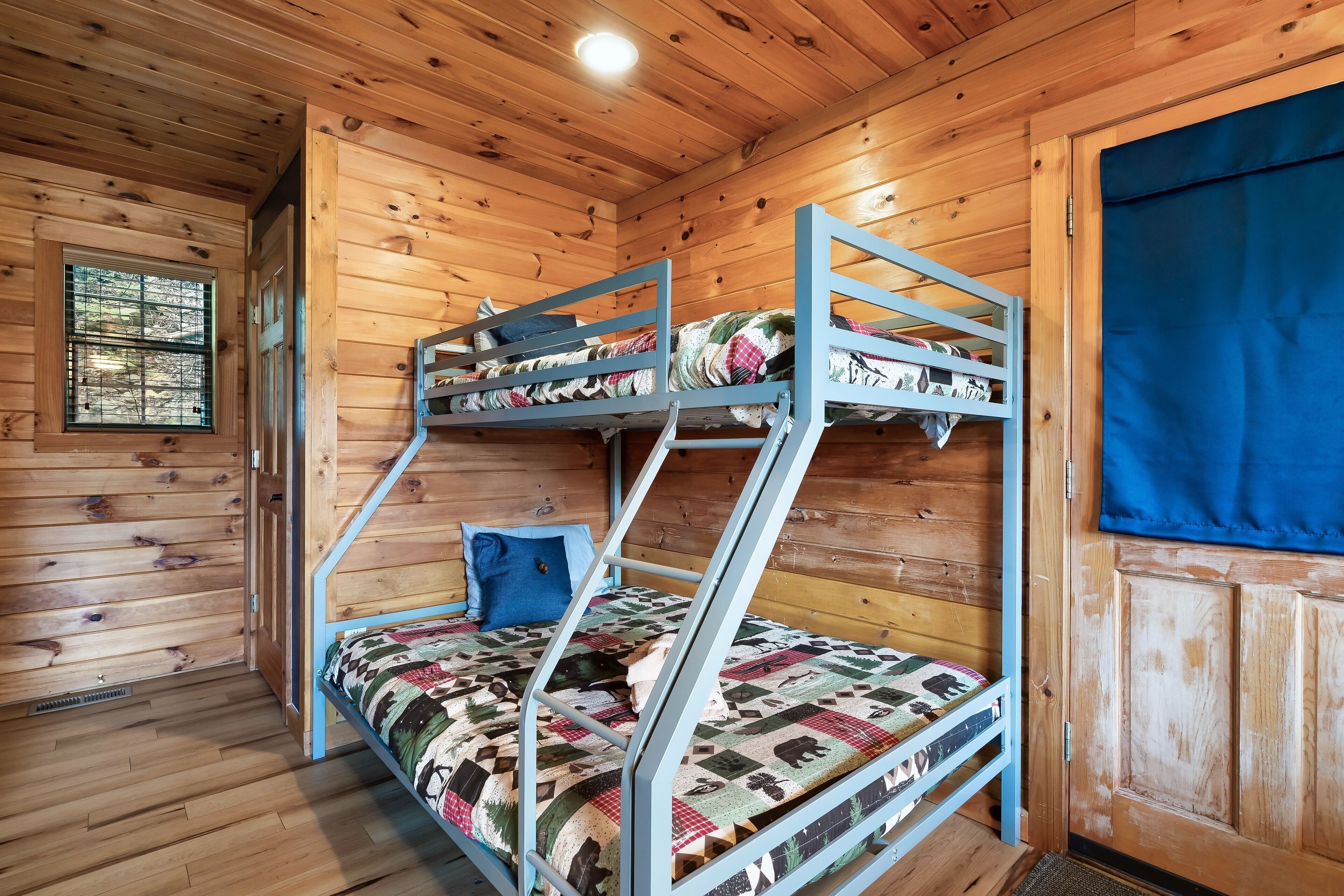 A bunk bed with a quilted bedspread, a blue pillow, and a wooden cabin interior with a window and a door.