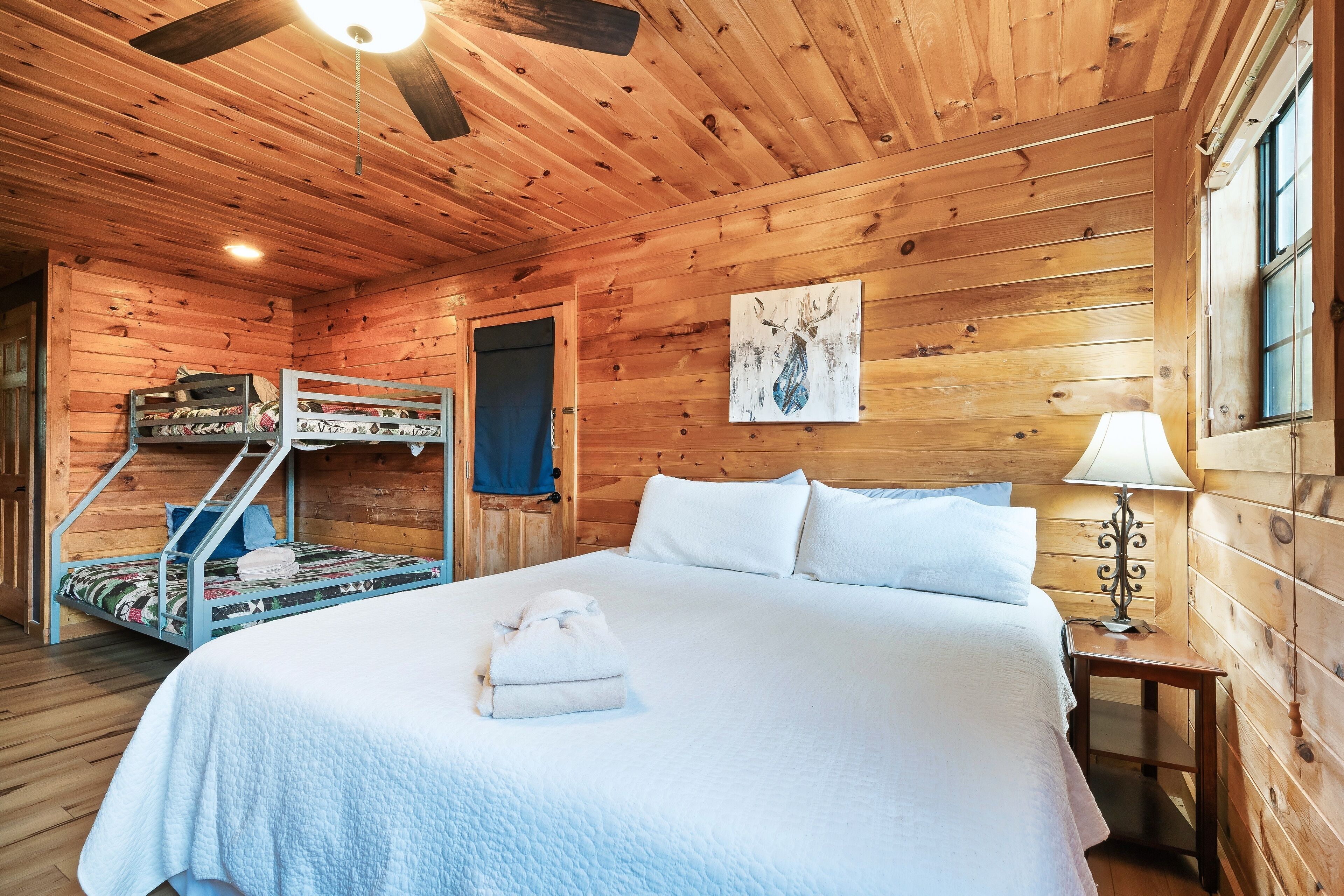 Una habitación tipo cabaña de madera con una litera, una cama grande y un ventilador de techo.