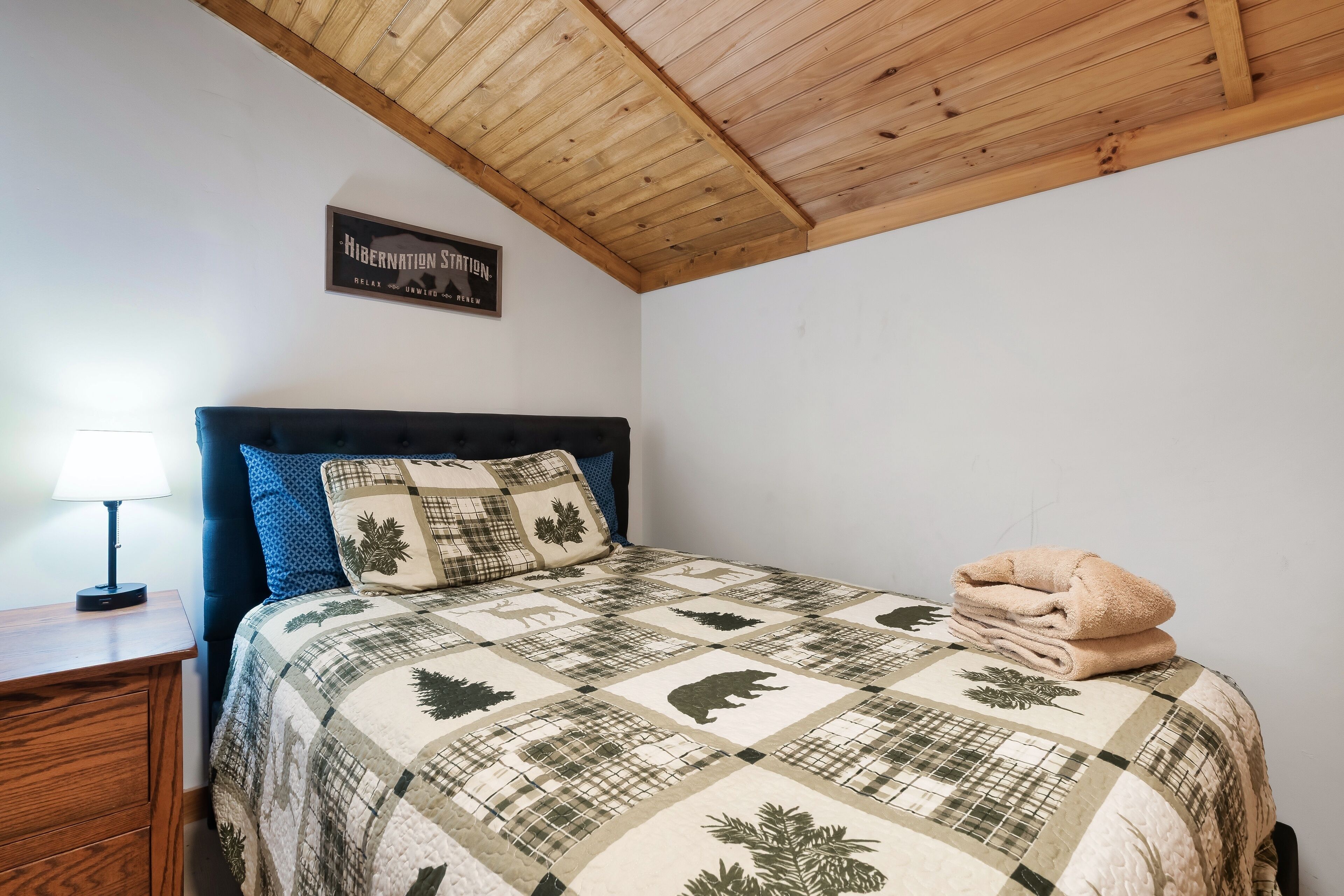 Une chambre à coucher avec un lit, une table de chevet, une lampe et un plafond en bois.