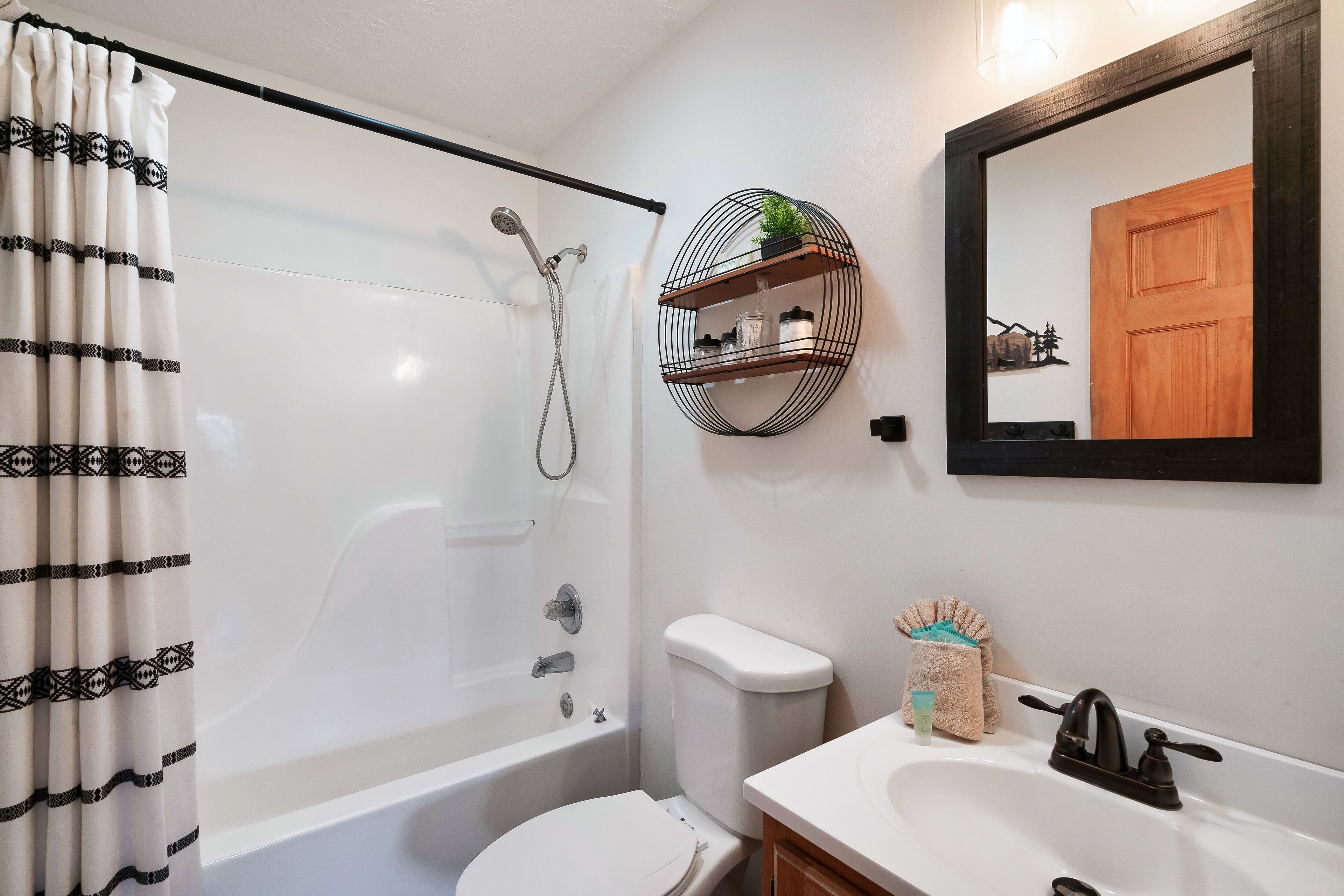 Een badkamer met een badkuip, toilet, wastafel en een spiegel met weerspiegeling van een houten deur.