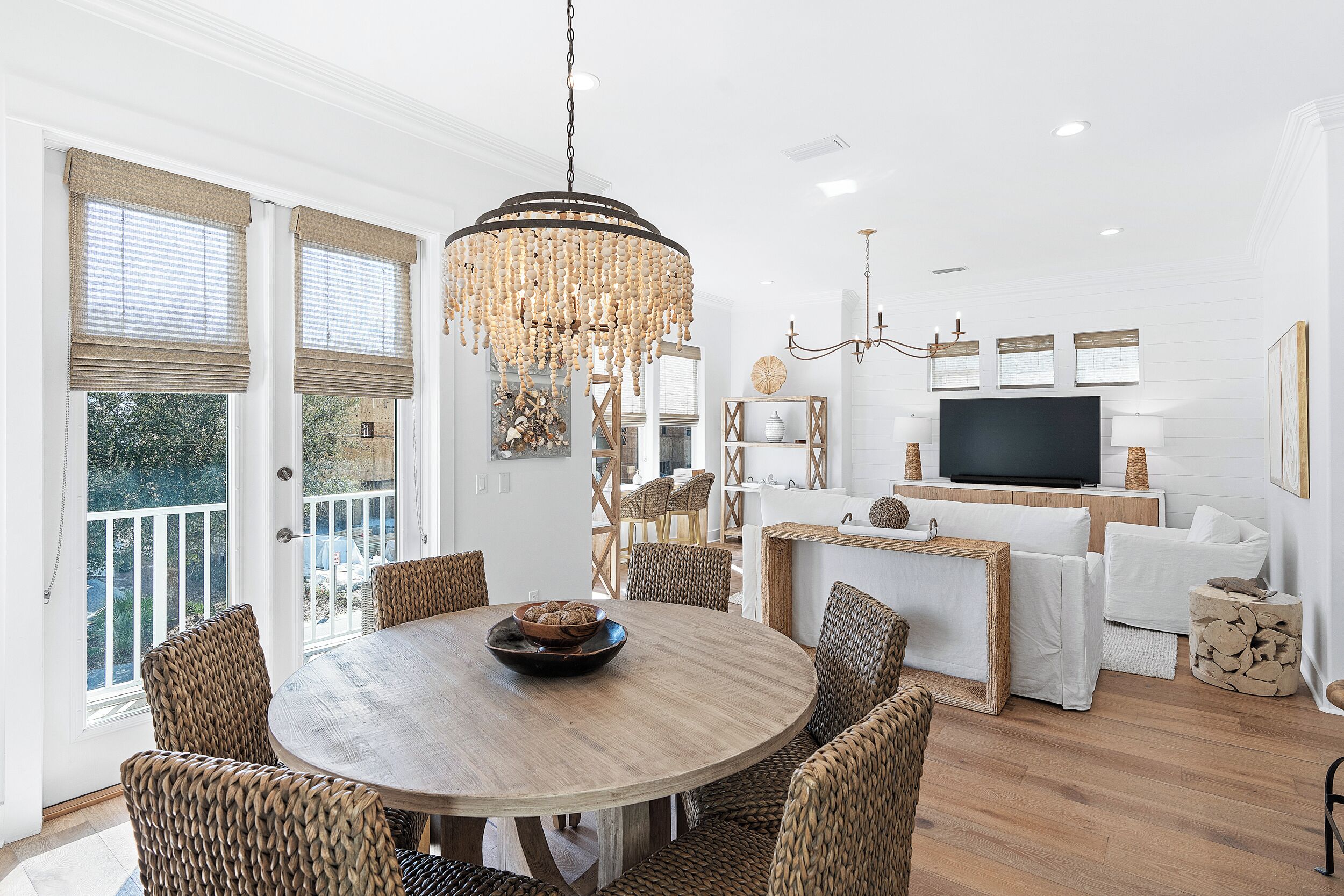 A dining area with a round wooden table, wicker chairs, a chandelier, and a television in the background.