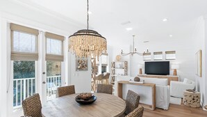 Ein Essbereich mit einem runden Holztisch, Korbstühlen, einer Chandelüster und einem Fernseher im Hintergrund.