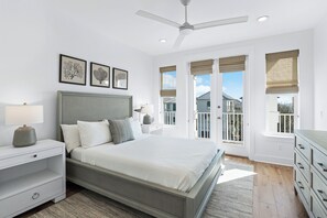 Une chambre à coucher comprenant un lit, des tables de chevet, une commode, un ventilateur de plafond et un balcon avec des fenêtres.