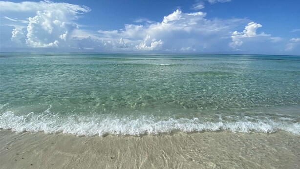 Ein Strand mit klarem türkisblauem Wasser und sanften Wellen.