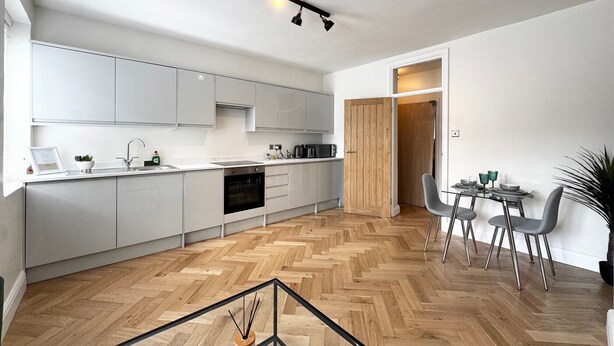 A modern kitchen with white cabinets, a herringbone wood floor, and a dining area with a glass table and chairs. - Heart of London Bridge - Central (London)