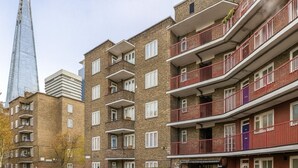 A multi-story residential building with balconies, brick facade, and a modern skyscraper in the background. - Heart of London Bridge - Central (London)