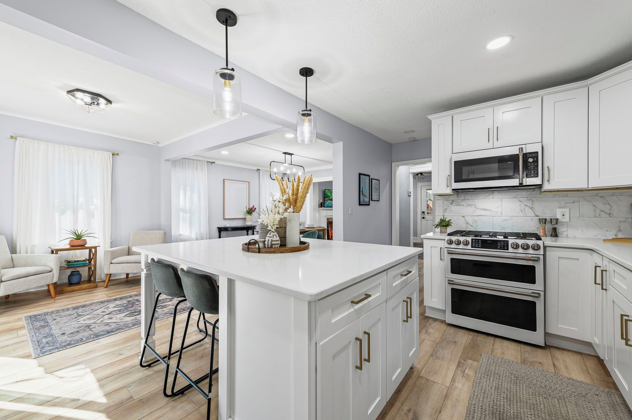 A modern kitchen with white cabinetry, a central island, a double oven, and a microwave.