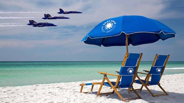 En strand med en blå parasol og to liggestole.