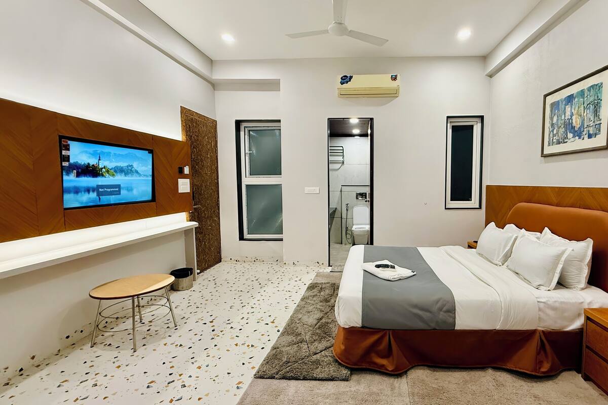 Una habitación de hotel moderna con cama, televisión, una mesita y zona de ducha.