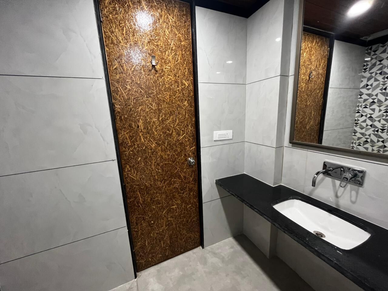 A modern bathroom with a wooden door, a black countertop, and a white sink.