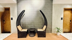 Une pièce comprenant deux fauteuils en osier à haut dossier avec des coussins beige, une petite table ronde et une plante en pot.