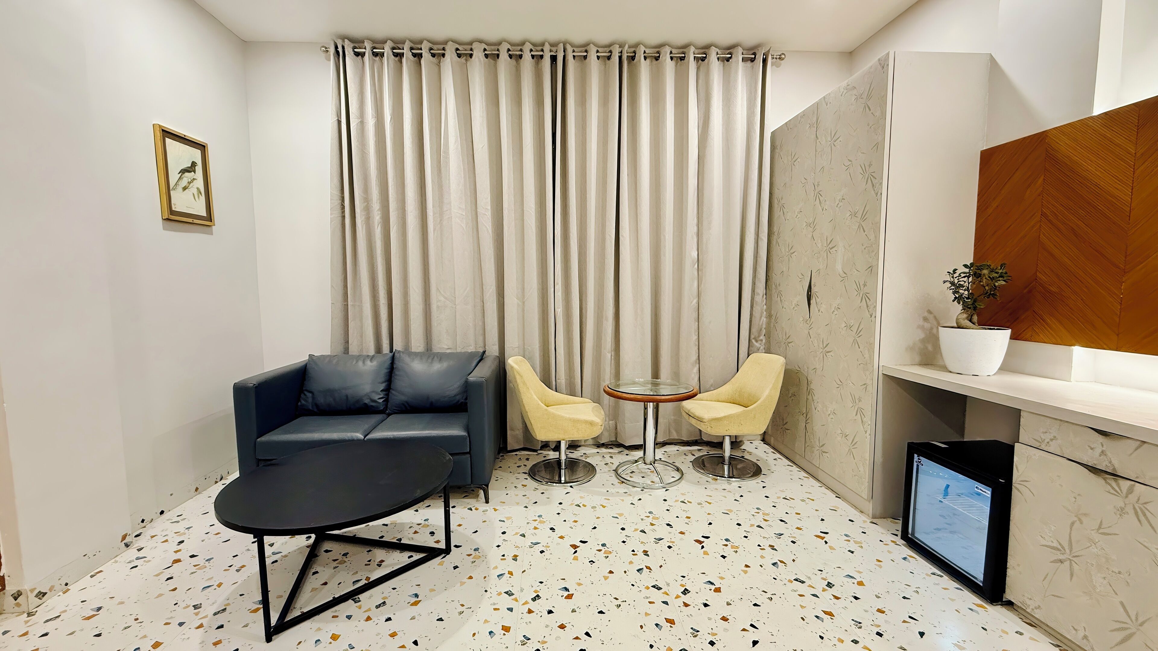A compact living space with a black sofa, two yellow chairs, a small round table, and a TV on a wooden shelf.