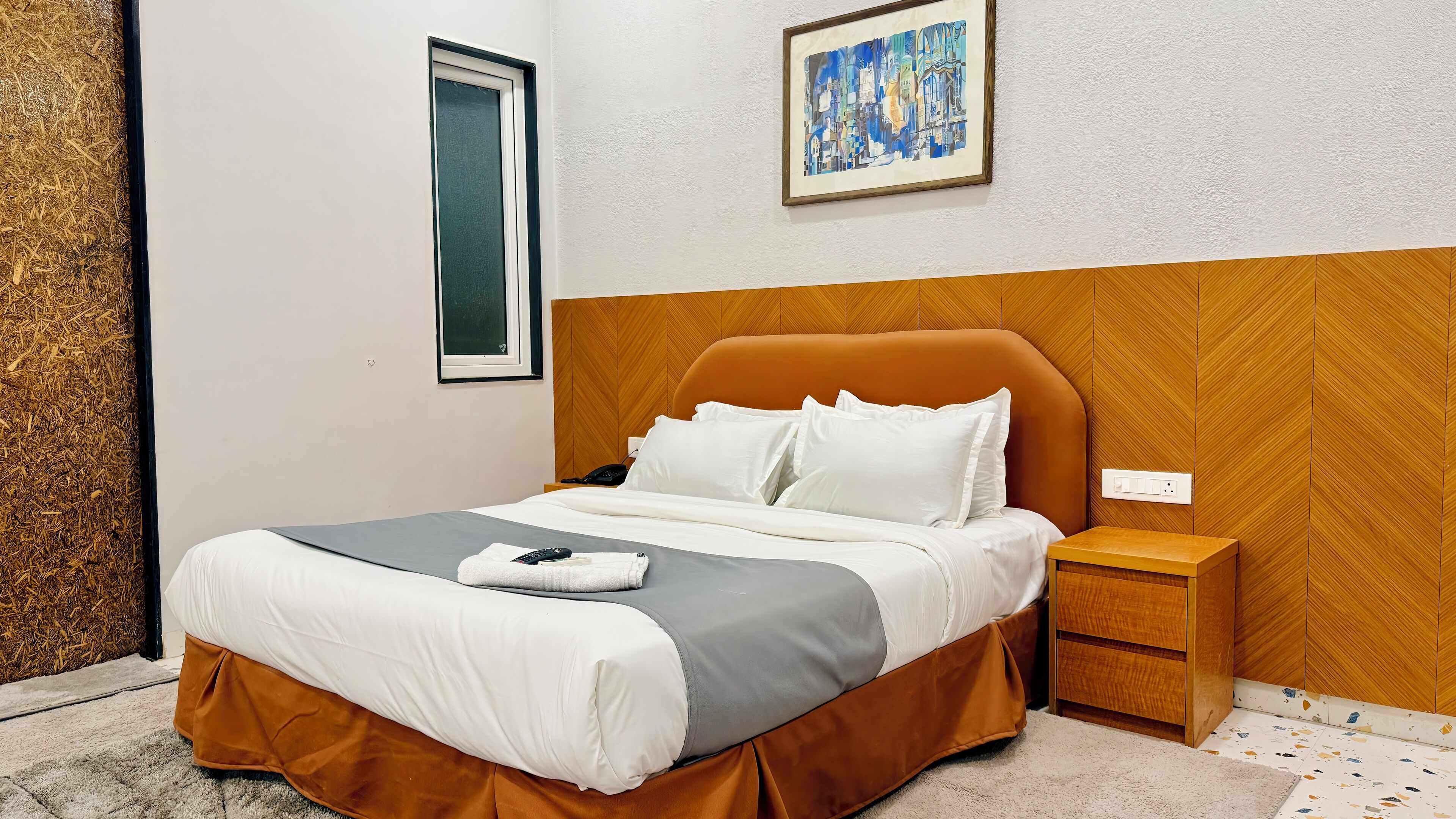 A neatly made bed with white and gray bedding, a brown headboard, and a bedside table with a lamp.