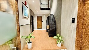 Un couloir doté d’un plancher en bois, de deux plantes en pot, d’un fauteuil suspendu noir et d’une porte sur laquelle figure un numéro.