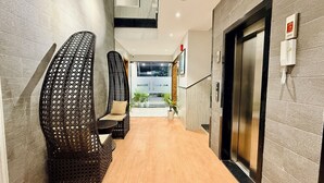 Un couloir avec des fauteuils en osier, un comptoir d’accueil et un ascenseur.