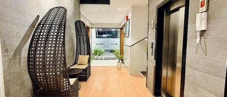 A hallway with wicker chairs, a reception desk, and an elevator.