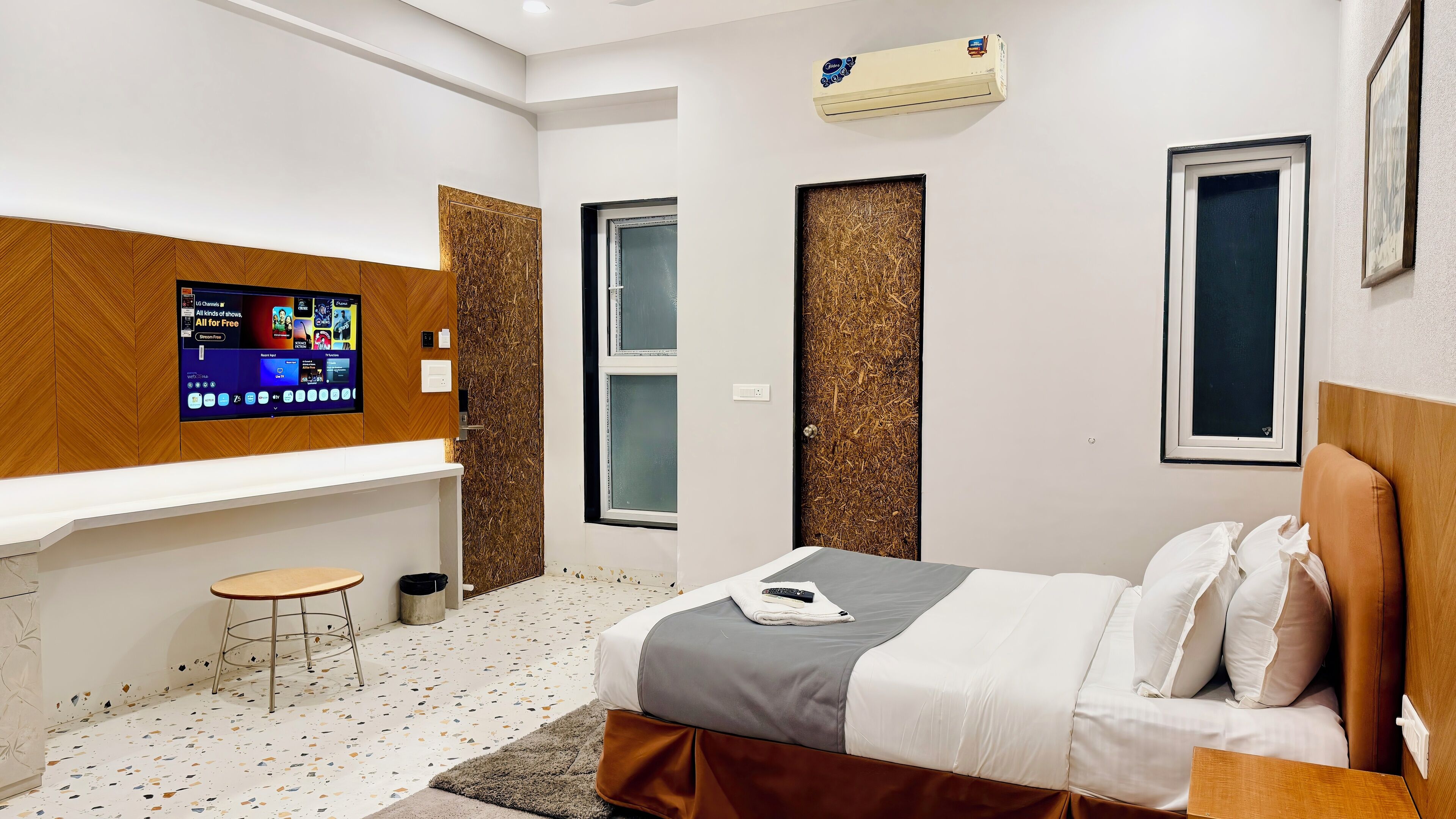 A modern hotel room with a bed, a small desk, a TV mounted on the wall, and a window.