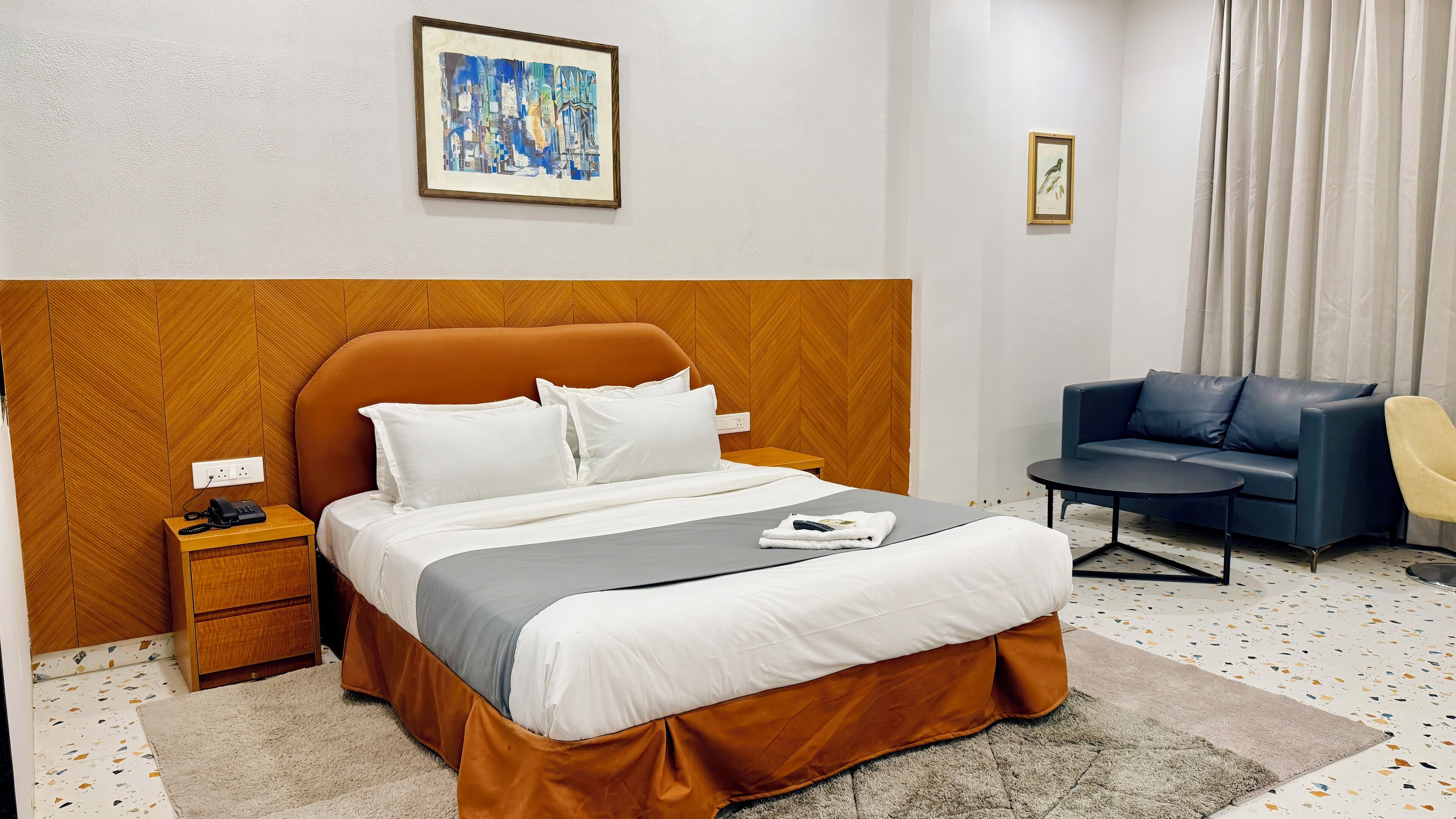 A hotel room with a bed, a bedside table with a phone, a sofa, and a chair.