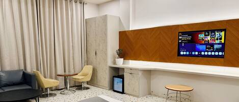 Een moderne hotelkamer met een bed, een bank, twee fauteuils, een bijzettafeltje, een televisie en een plant.