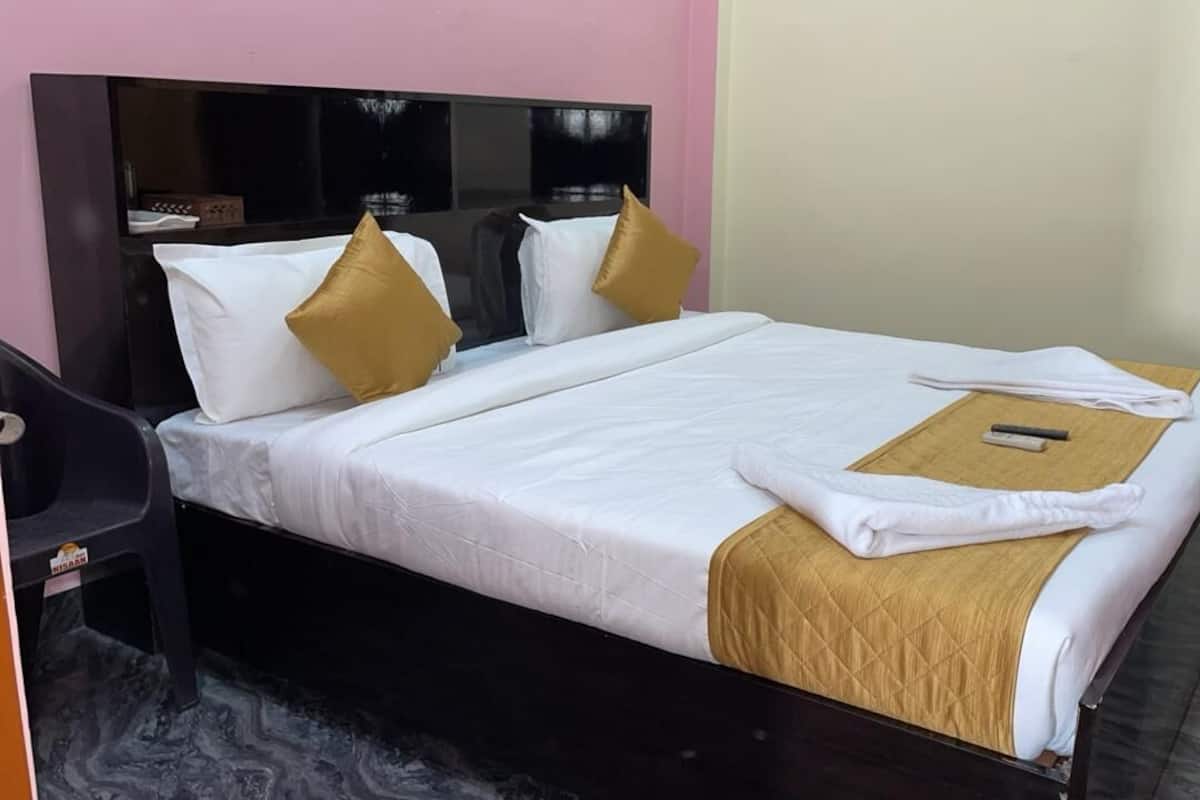 Una cama bien hecha con ropa de cama blanca y dorada, un cabecero de madera y una mesita de noche con una silla.
