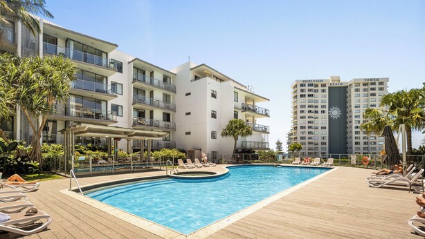 Un hotel moderno con piscina en la azotea, varios balcones y vistas a un edificio alto identificado como "Burleigh Beach Tower".