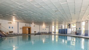 A large indoor swimming pool with a tiled floor, a wooden locker area, and a staircase leading to an upper level. - Valley Lodge 61 (Gunnislake)