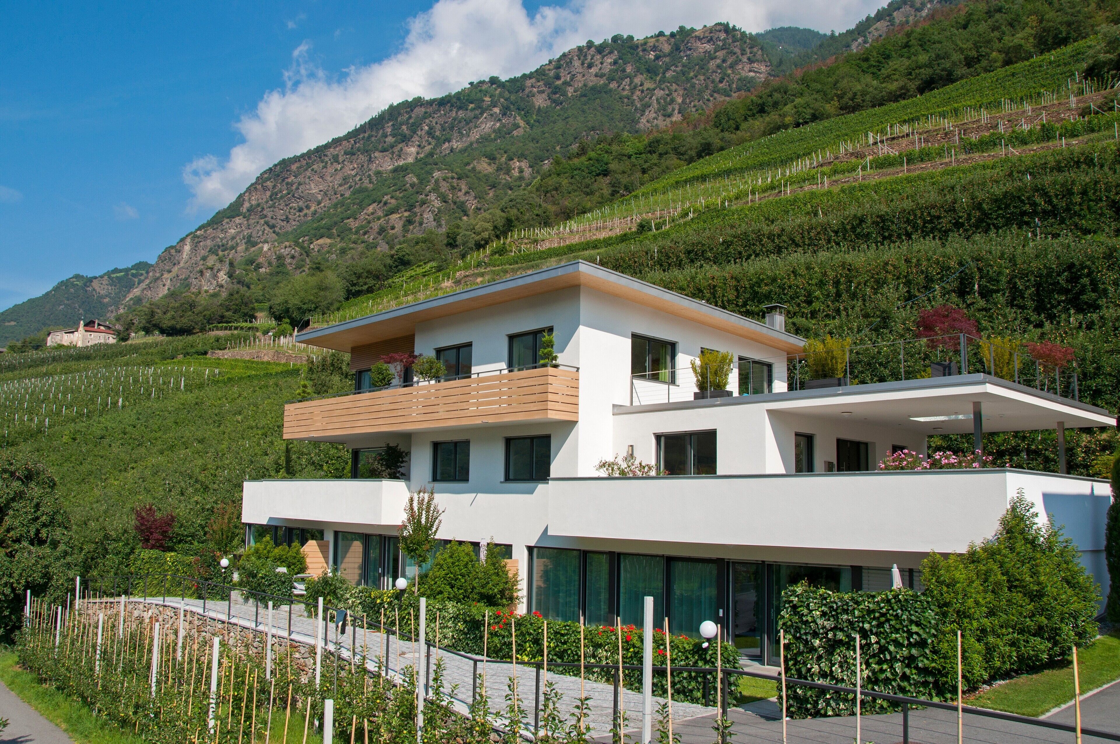 Ein modernes, zweistöckiges Haus mit flachem Dach, großen Fenstern und einem Balkon.