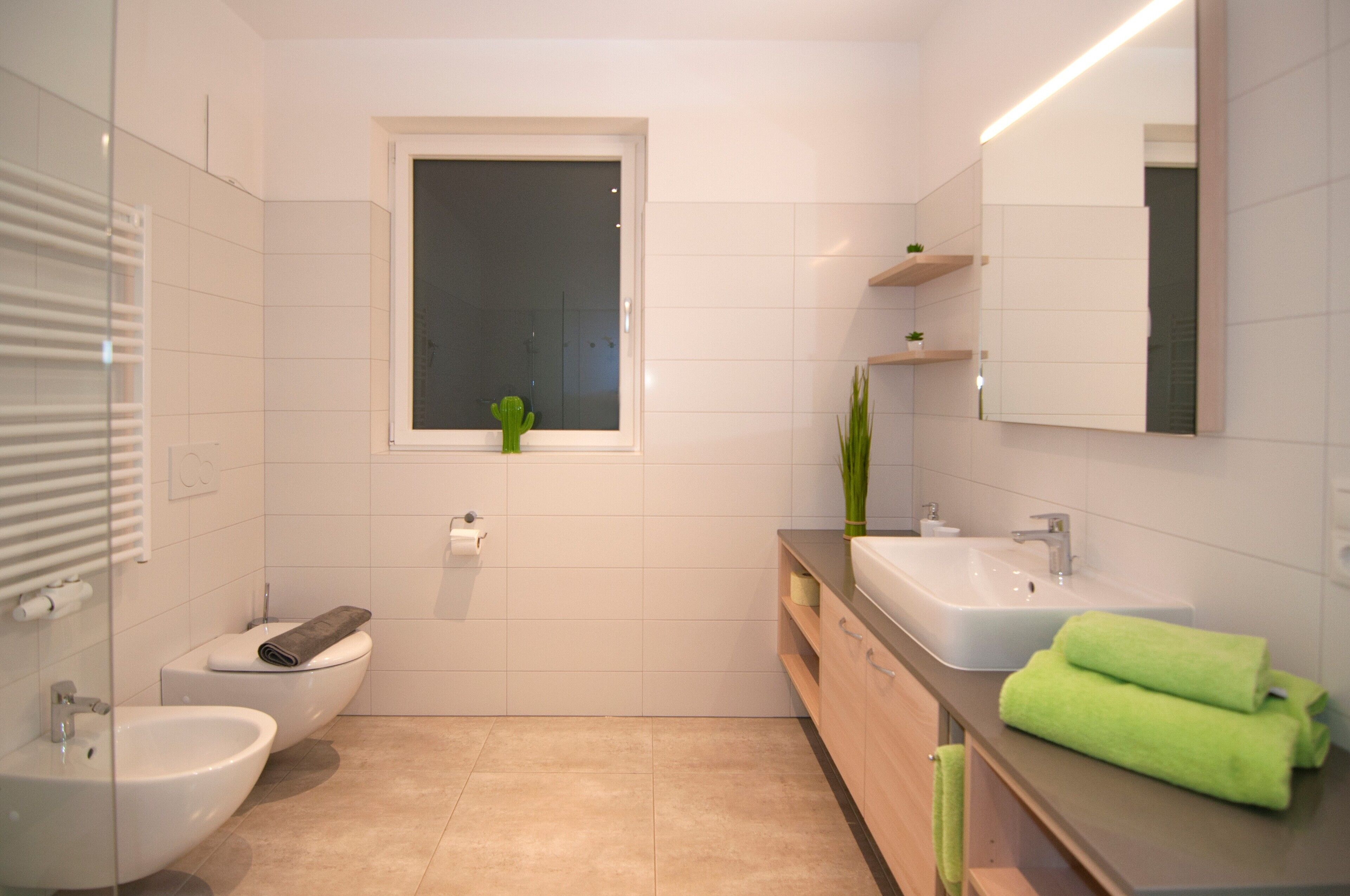 Une salle de bain moderne équipée d’un bidet, de toilettes, d’un lavabo et d’une fenêtre avec un cactus.