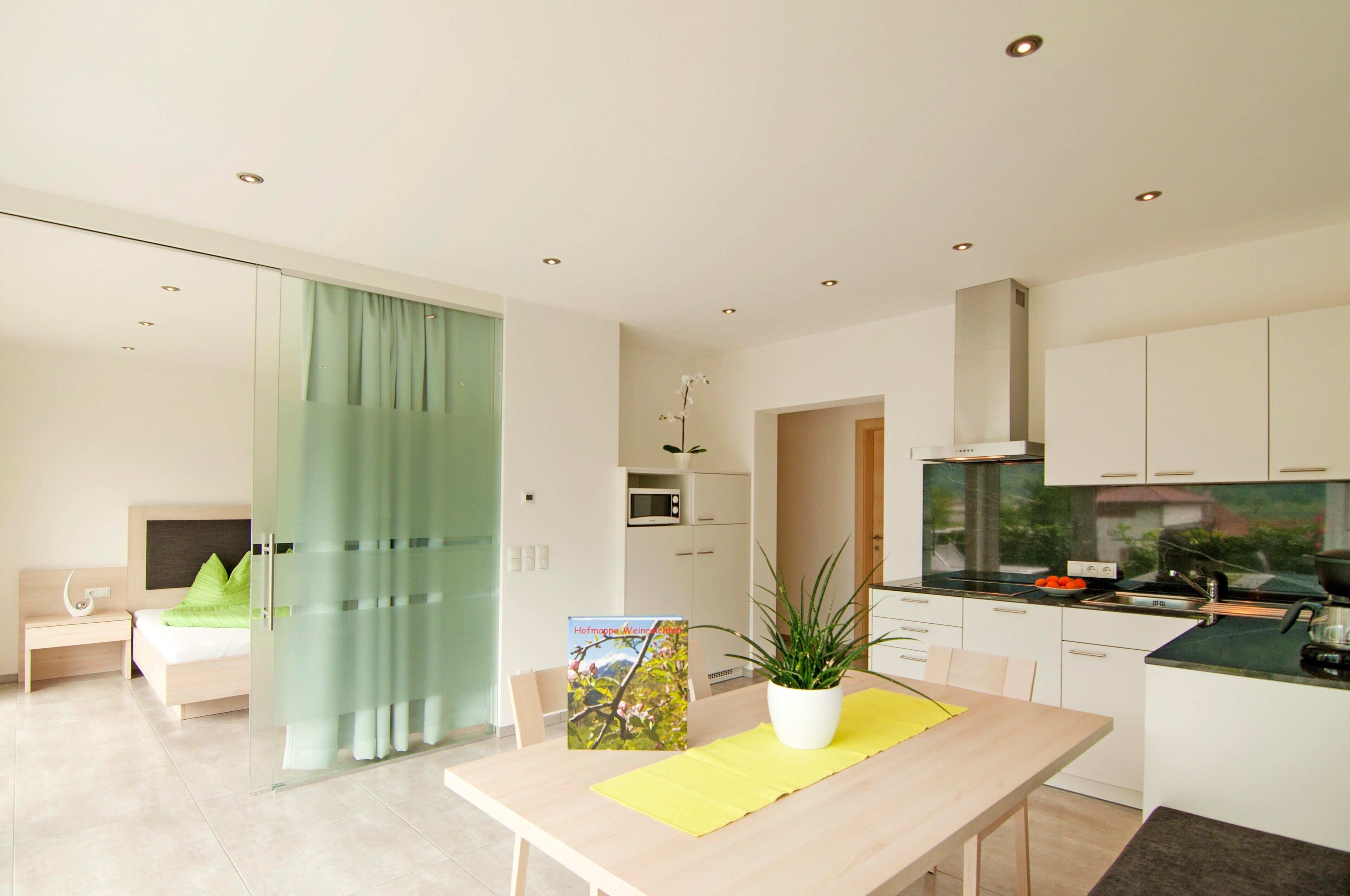 A modern kitchen with a microwave, stove, and sink. There is a dining table with a potted plant and a book.