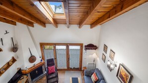 Una habitación con techos altos, vigas de madera, chimenea, sofá, televisor y tragaluz.