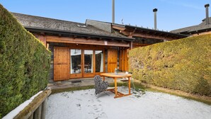 Una cabaña de madera con un patio cubierto de nieve, una mesa con sillas y un ventanal grande.