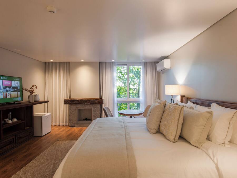 A hotel room with a bed, a TV, a fireplace, a window with a view, and a lamp.