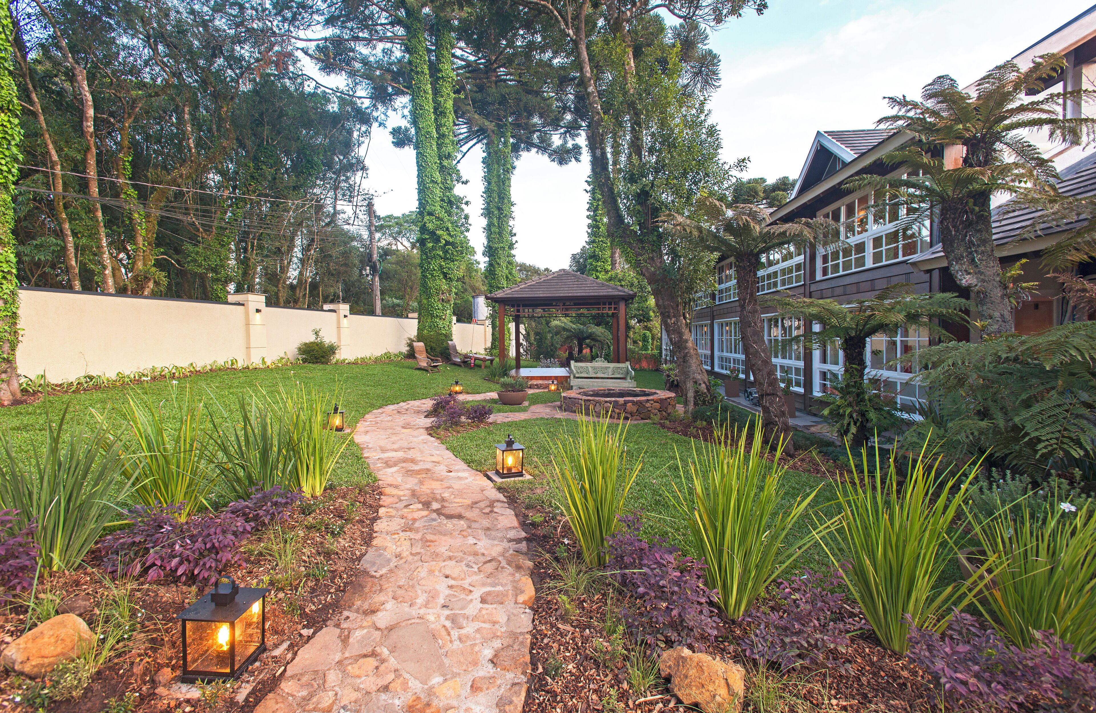 A garden pathway leading to a gazebo, surrounded by lush greenery and a stone wall.