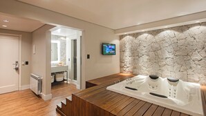 A modern bathroom with a wooden bench, a stone wall, and a mounted TV. - Varanda Boutique Hotel (Gramado)
