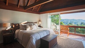 A bedroom with a large bed, a wooden nightstand, a bedside table, a bench, and a balcony with a view of the landscape. - Varanda Boutique Hotel (Gramado)